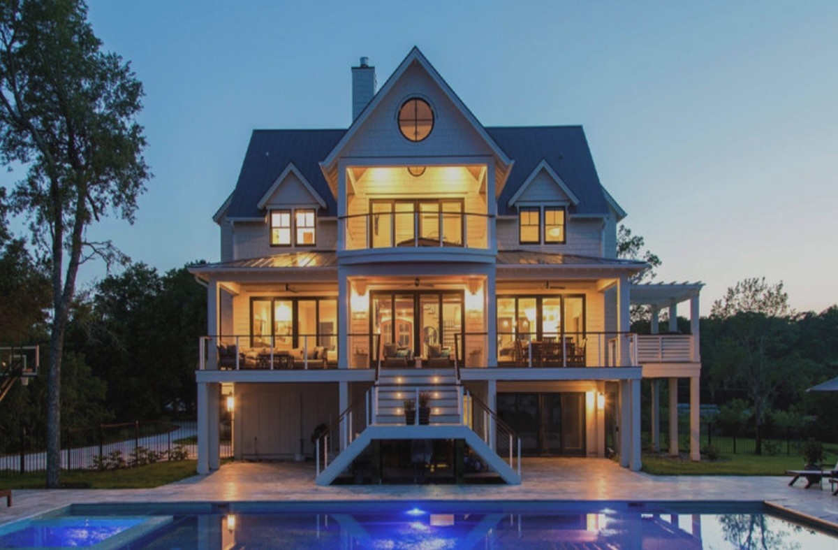 Brightly lit white house with pool at dusk
